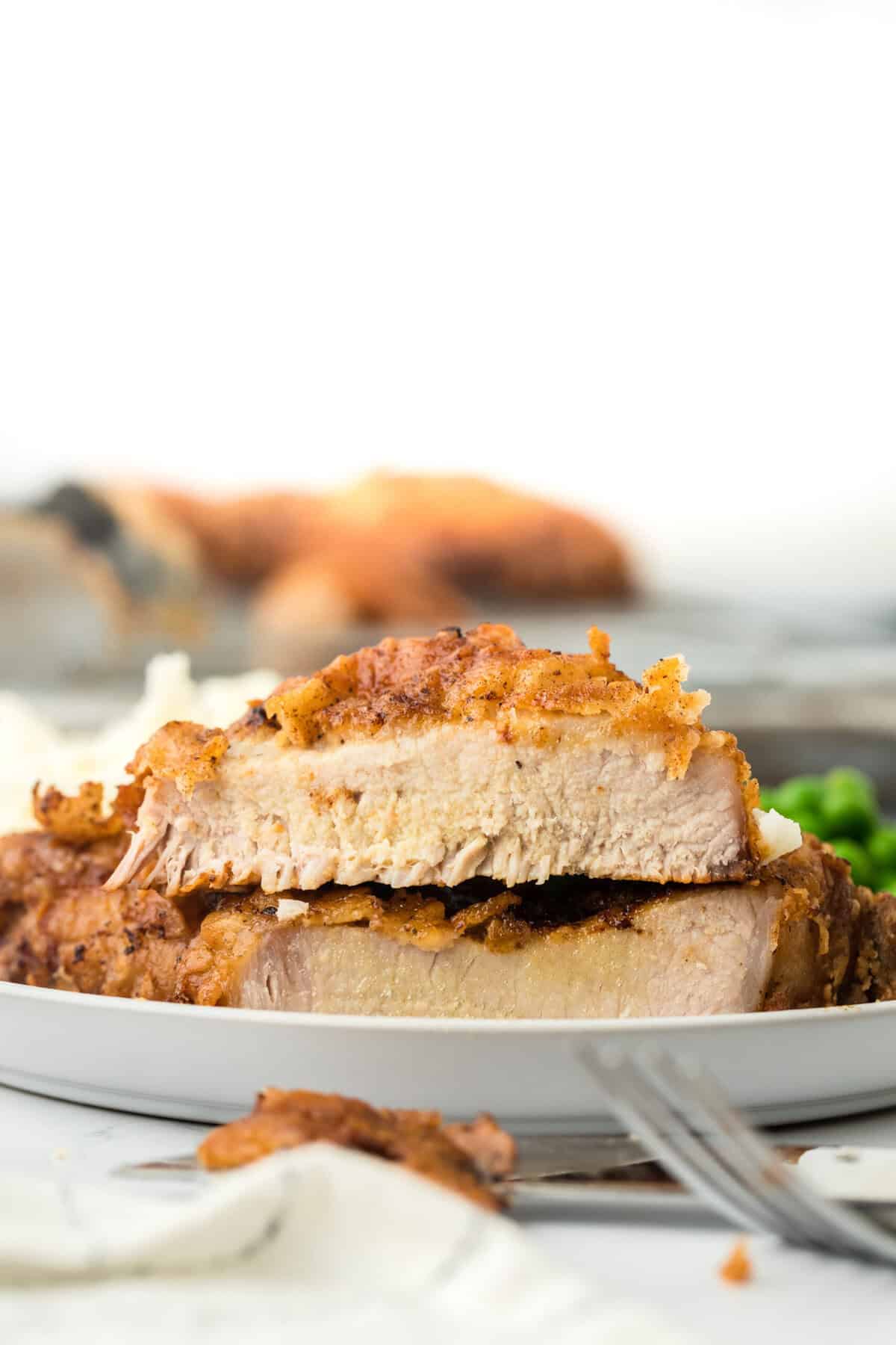 A southern fried pork chop cut in half to show the juicy texture inside on a white plate