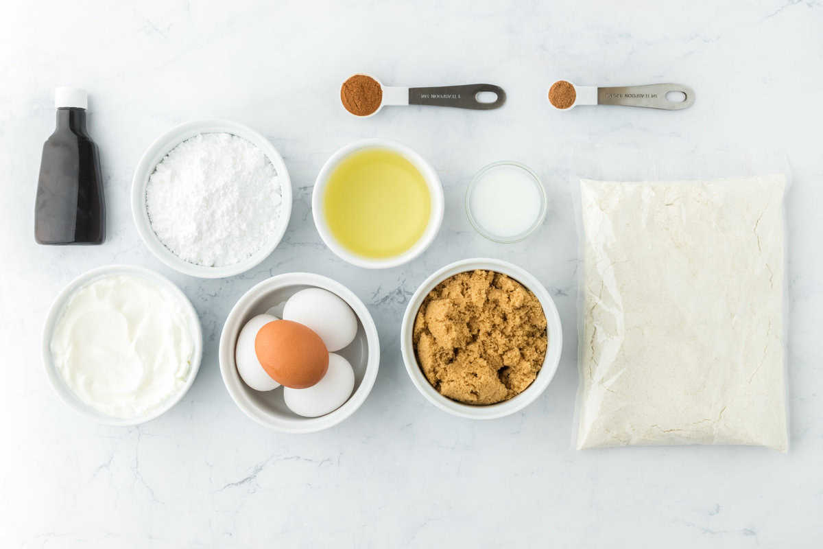 ingredients to make a honeybun cake like brown sugar, eggs, cake mix, oil and spices in white bowls