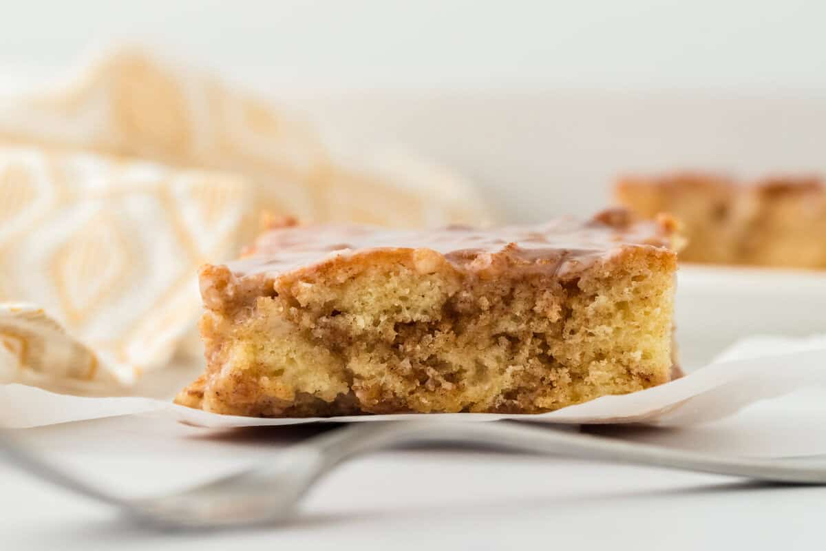 A slice of honey bun cake recipe on a white plate with a yellow napkin in the background