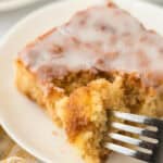 A slice of honey bun cake with a fork going into it to eat a piece on a white plate