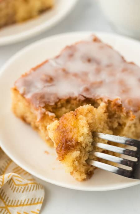 A slice of honey bun cake with a fork going into it to eat a piece on a white plate