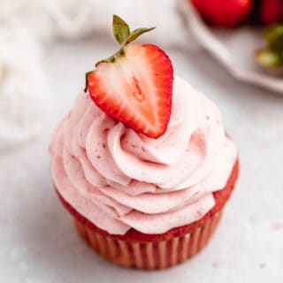 A strawberry cupcake against a white background with strawberries in the background