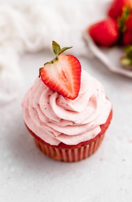 A strawberry cupcake against a white background with strawberries in the background