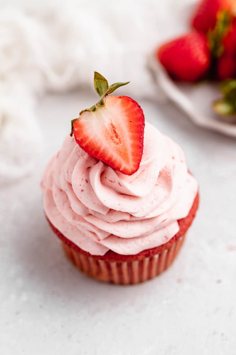 A strawberry cupcake against a white background with strawberries in the background