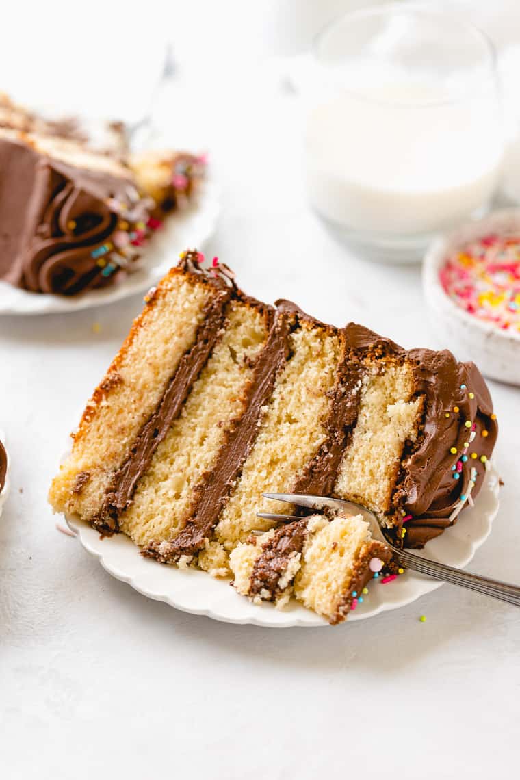 Two slices of yellow cake with chocolate frosting on plates with a fork in a tutorial of how to convert cake to cupcakes