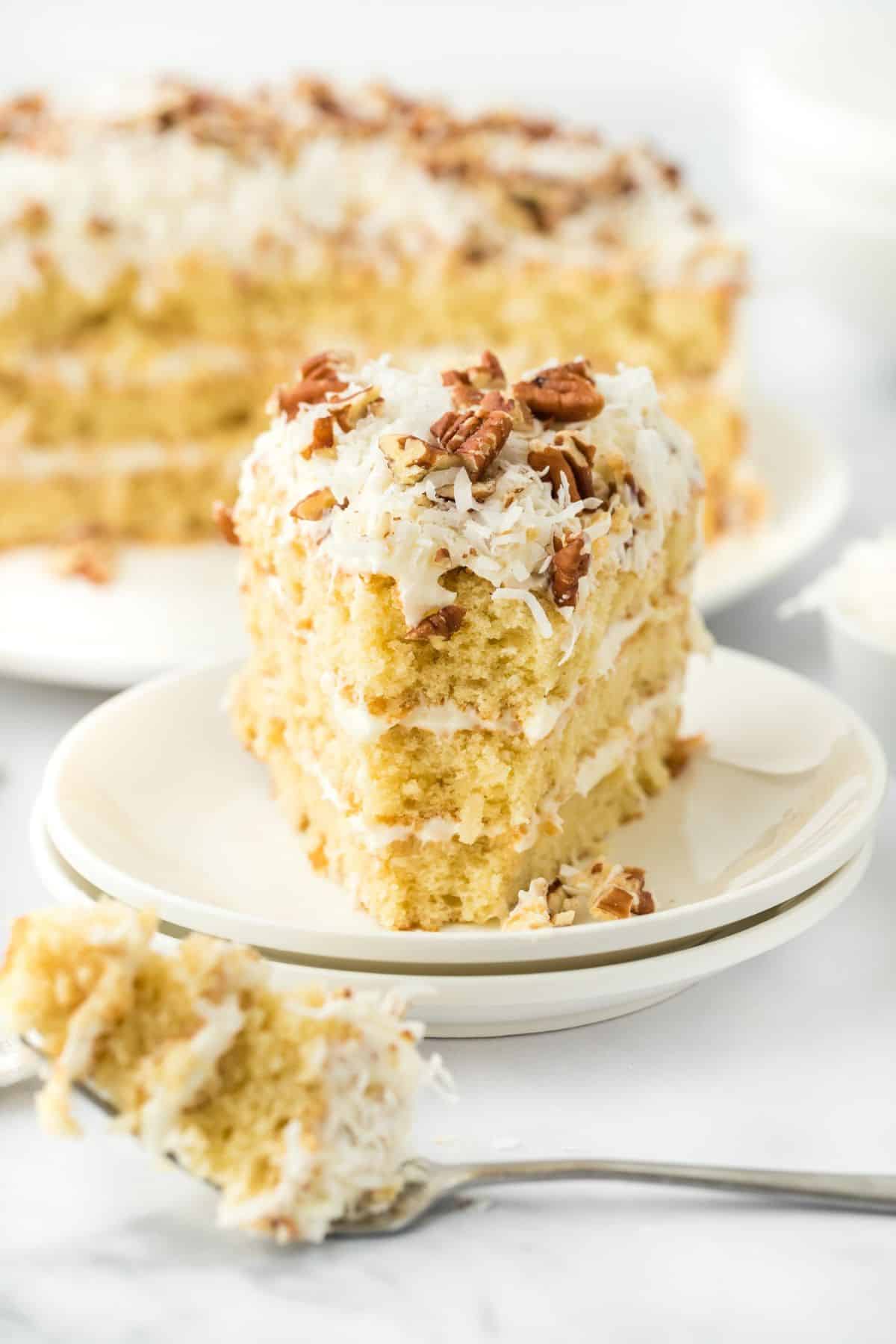 A slice of Italian cream cake, with a fork holding a small bite in the foreground and the rest of the cake in the background