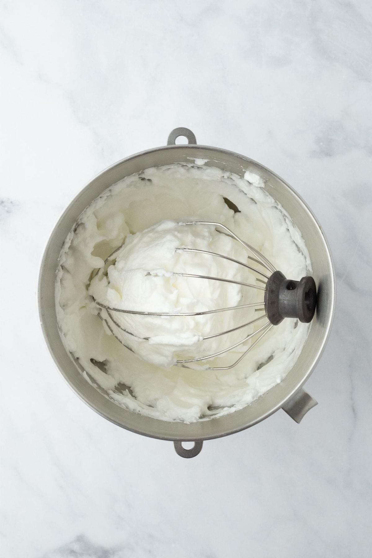 Fluffy whipped egg whites in a metal mixing bowl with a whisk attachment