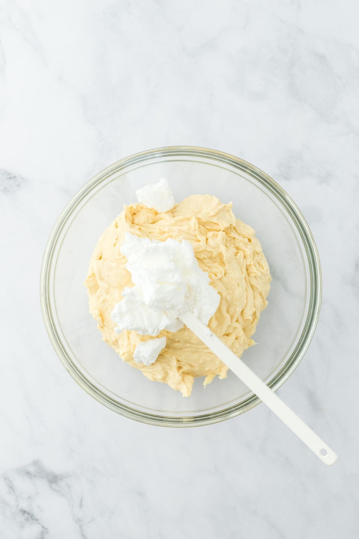 Whipped egg whites being gently folded into the cake batter in a clear glass bowl