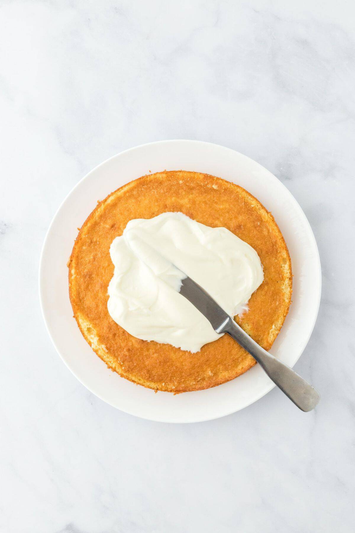 Cream cheese frosting being spread on the cake layer with a spatula