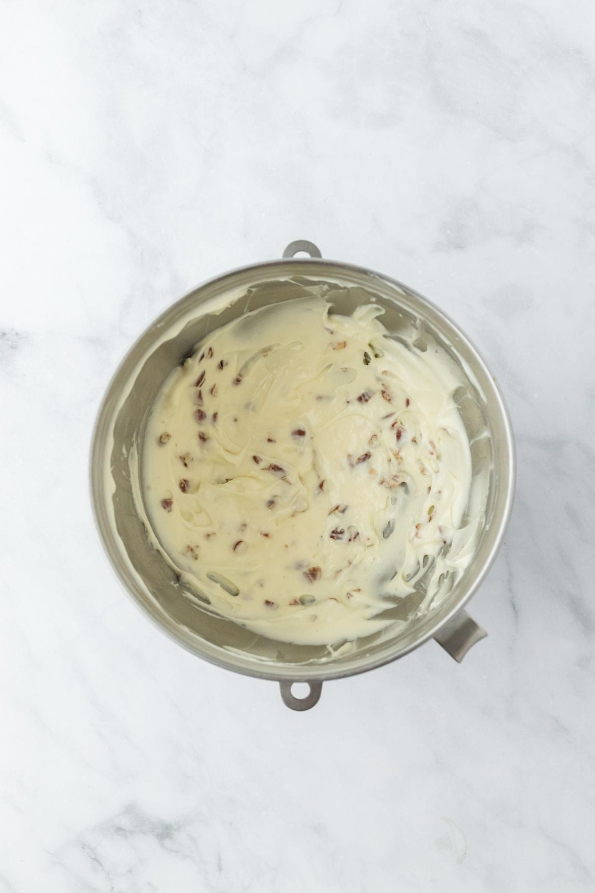 A mixing bowl with frosting mixed with chopped pecans