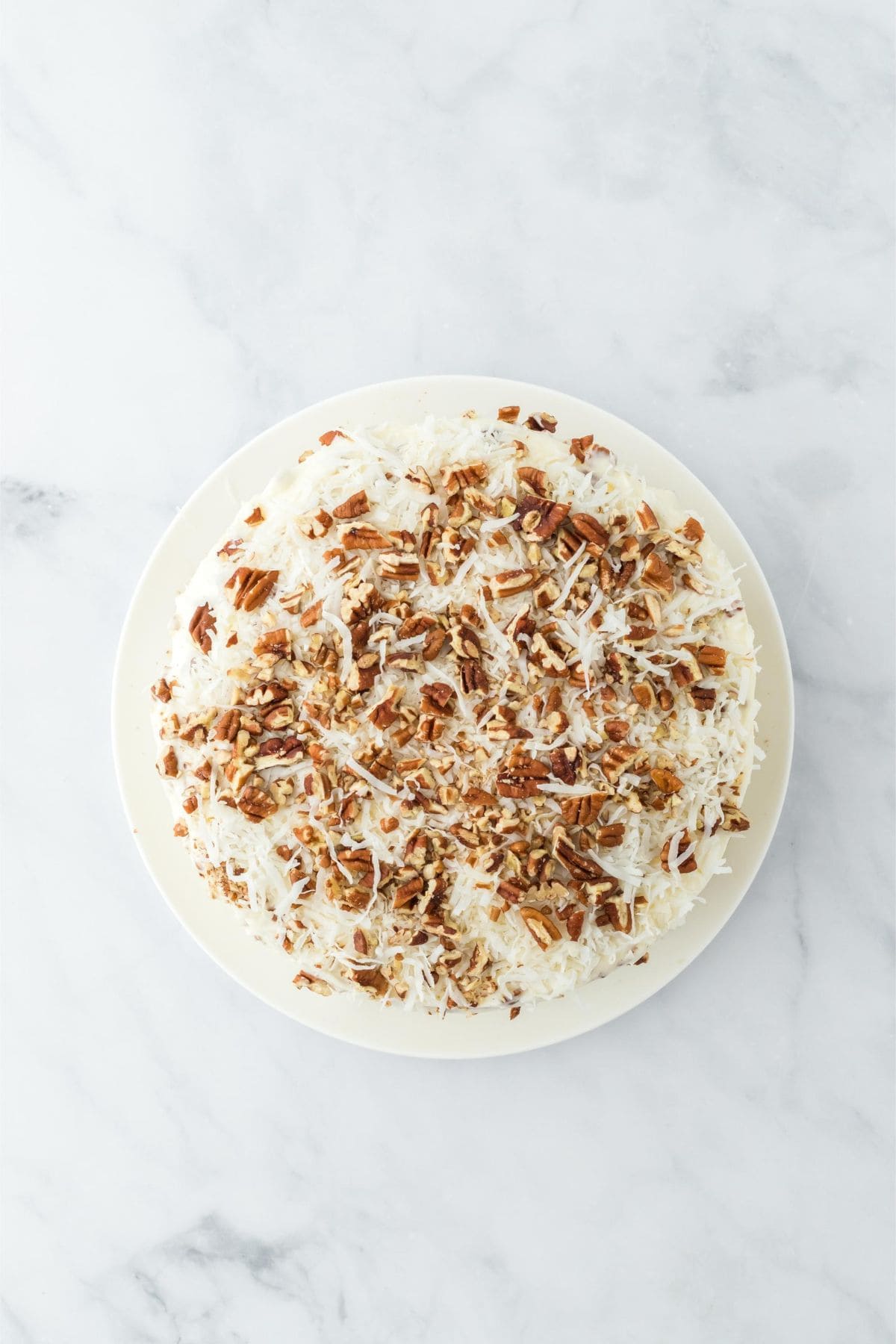 The cake fully frosted with more pecans and shredded coconut on top