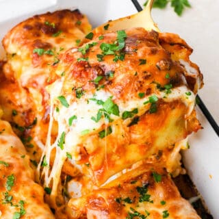 A close up of lasagna roll ups being pulled out of white pan