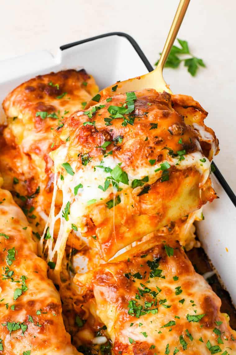 A close up of lasagna roll ups being pulled out of white pan