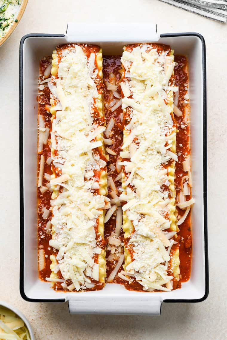 Chicken lasagna roll ups in a white pan with cheese on top before baking