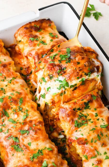 Spinach lasagna roll ups being taken out of a pan with cheese pulling after baked