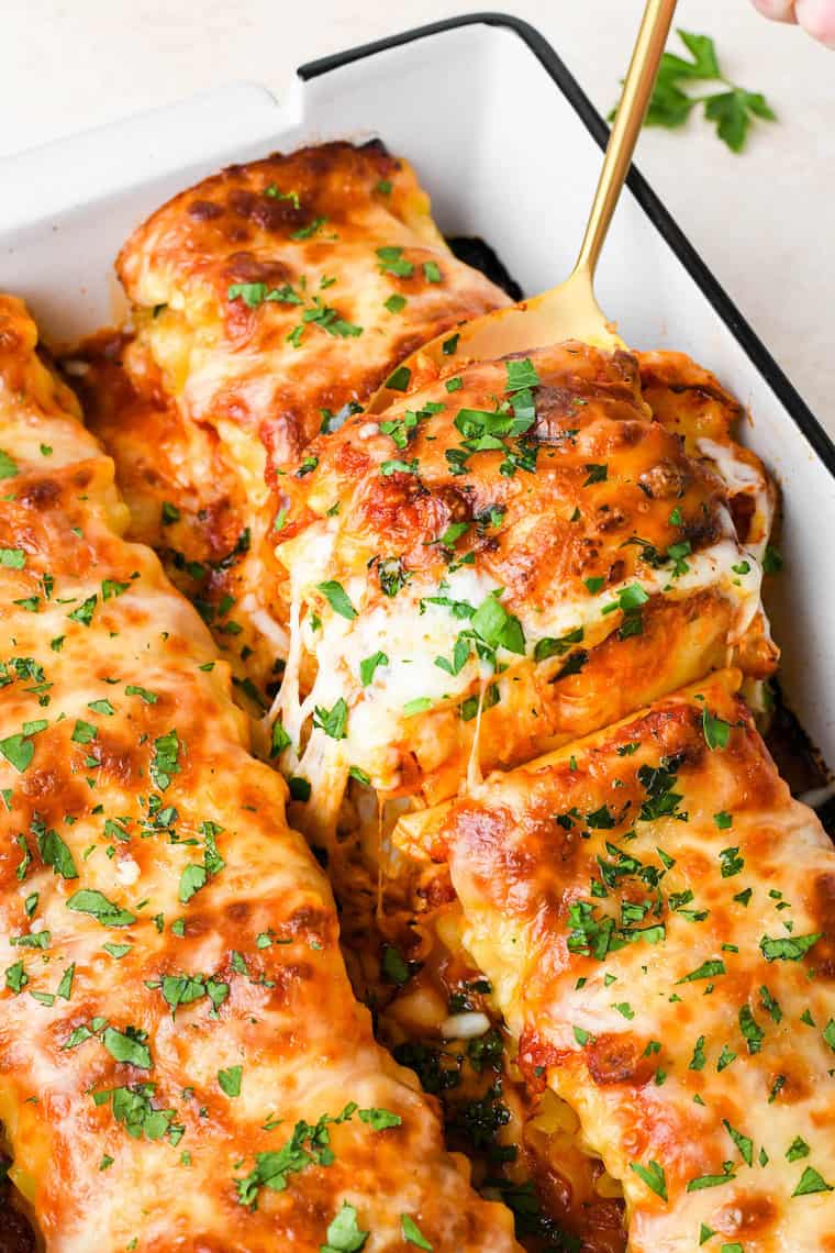 Spinach lasagna roll ups being taken out of a pan with cheese pulling after baked