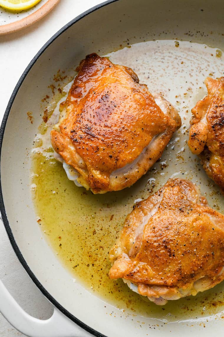 Three chicken thighs in a skillet being cooked until golden