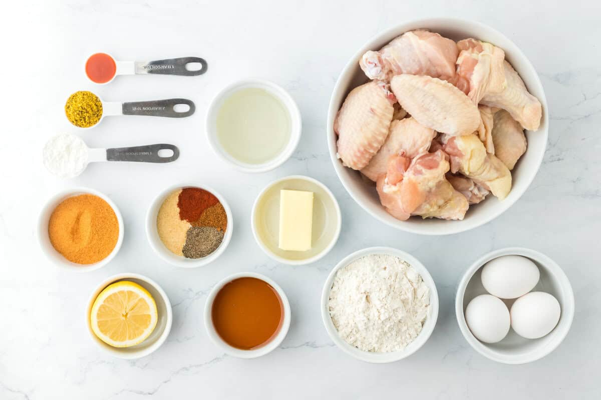 Chicken wings, seasonings, flour, and eggs in white bowls on white background