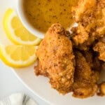 A close up of a lemon pepper chicken wings recipe on a white plate with lemon wedges and sauce on white background