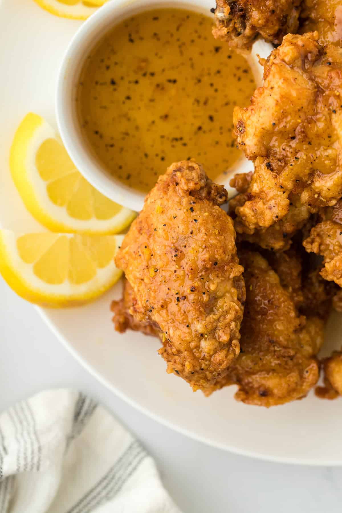 A close up of a lemon pepper chicken wings recipe on a white plate with lemon wedges and sauce on white background