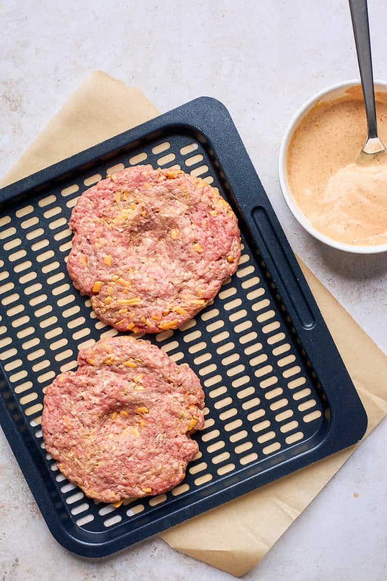 Two burger patties on an air fryer pan before baking