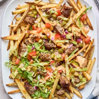 A white platter filled with loaded fries topped with cheeseburger toppings