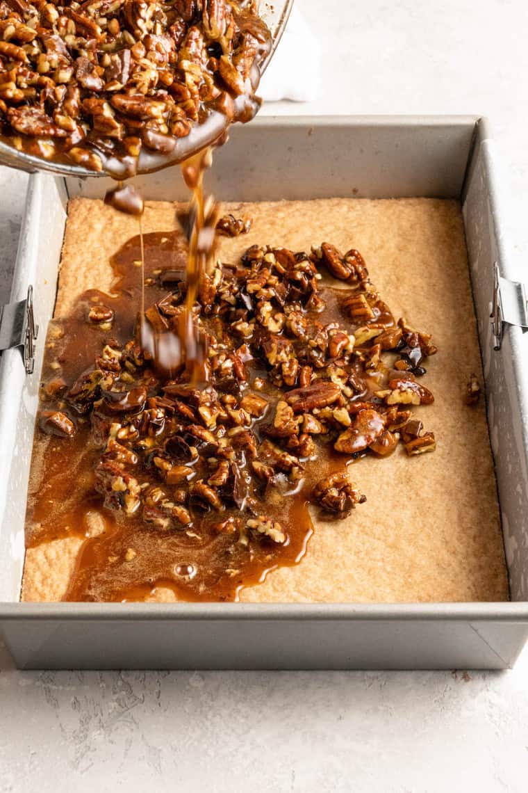 A chocolate pecan filling being poured over a shortbread crust