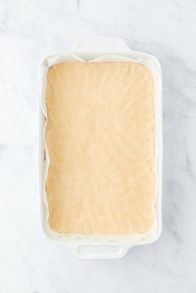 Shortbread crust pressed into a baking pan before baking on white background