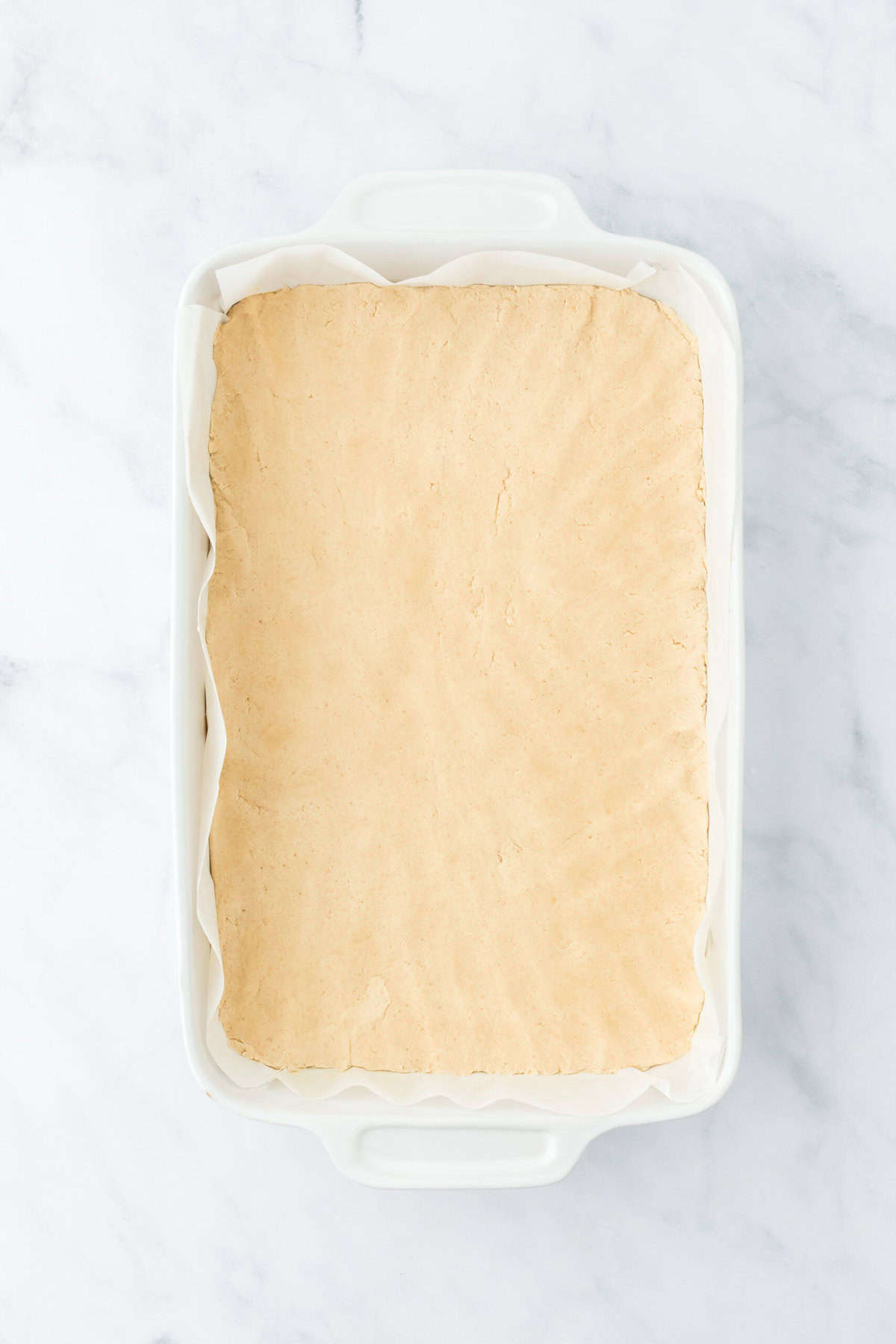 Shortbread crust pressed into a baking pan before baking on white background