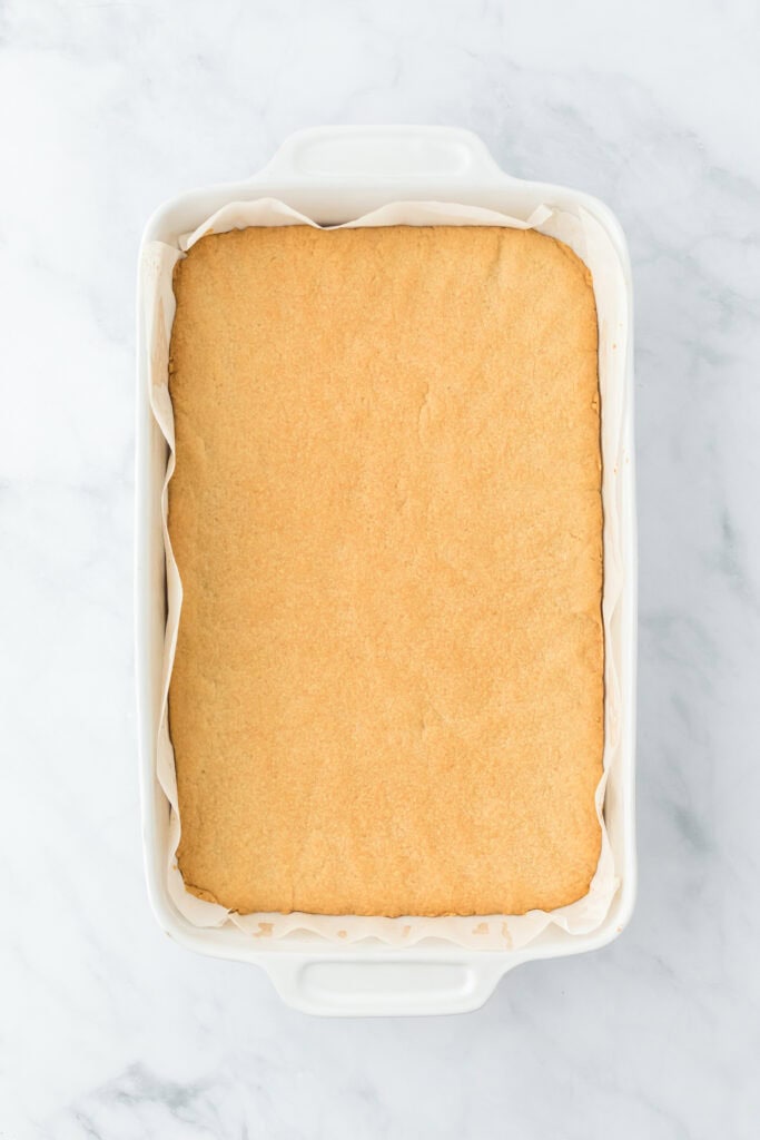 Baked shortbread crust in bottom of white baking pan on white background