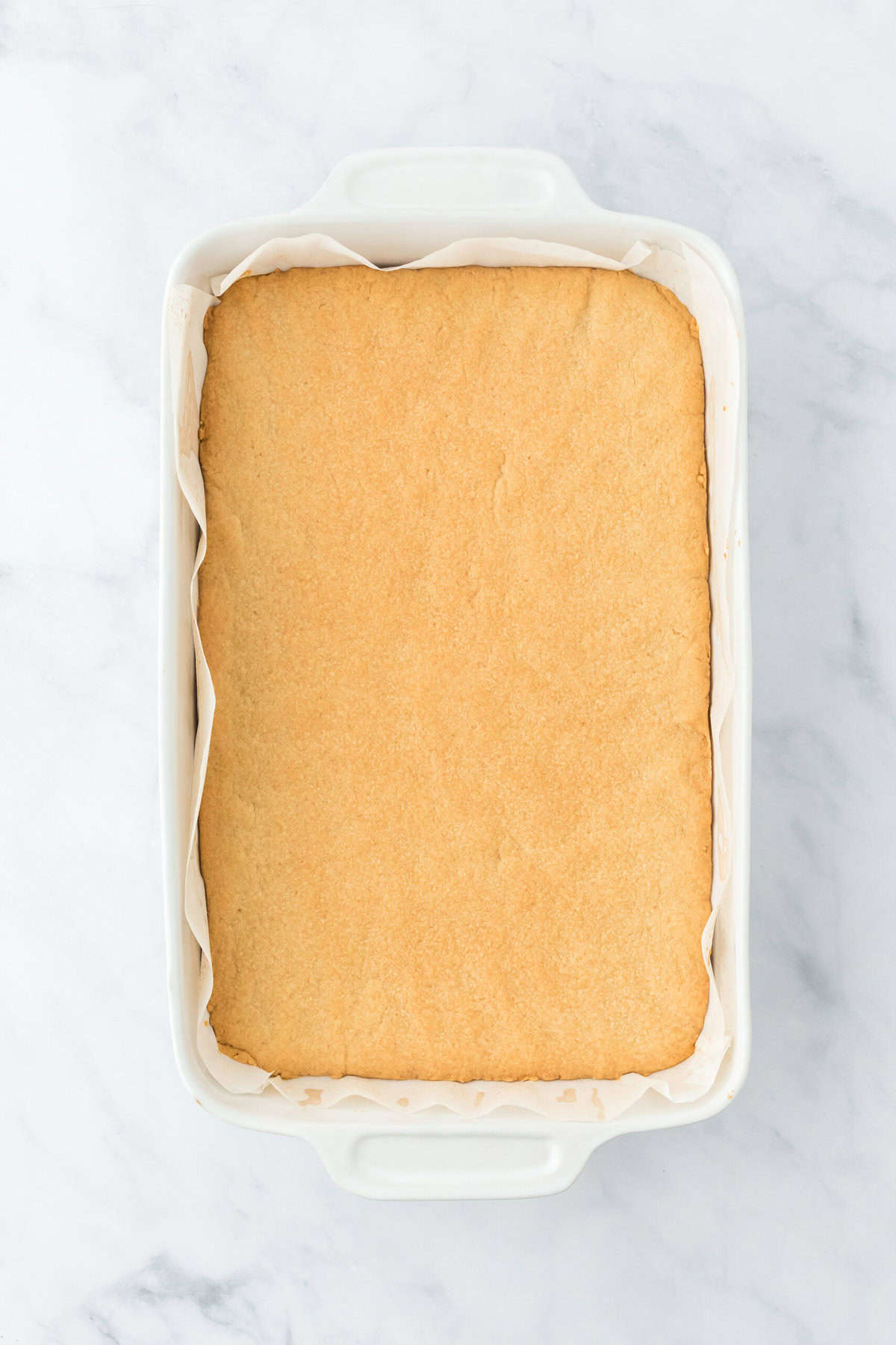 Baked shortbread crust in bottom of white baking pan on white background