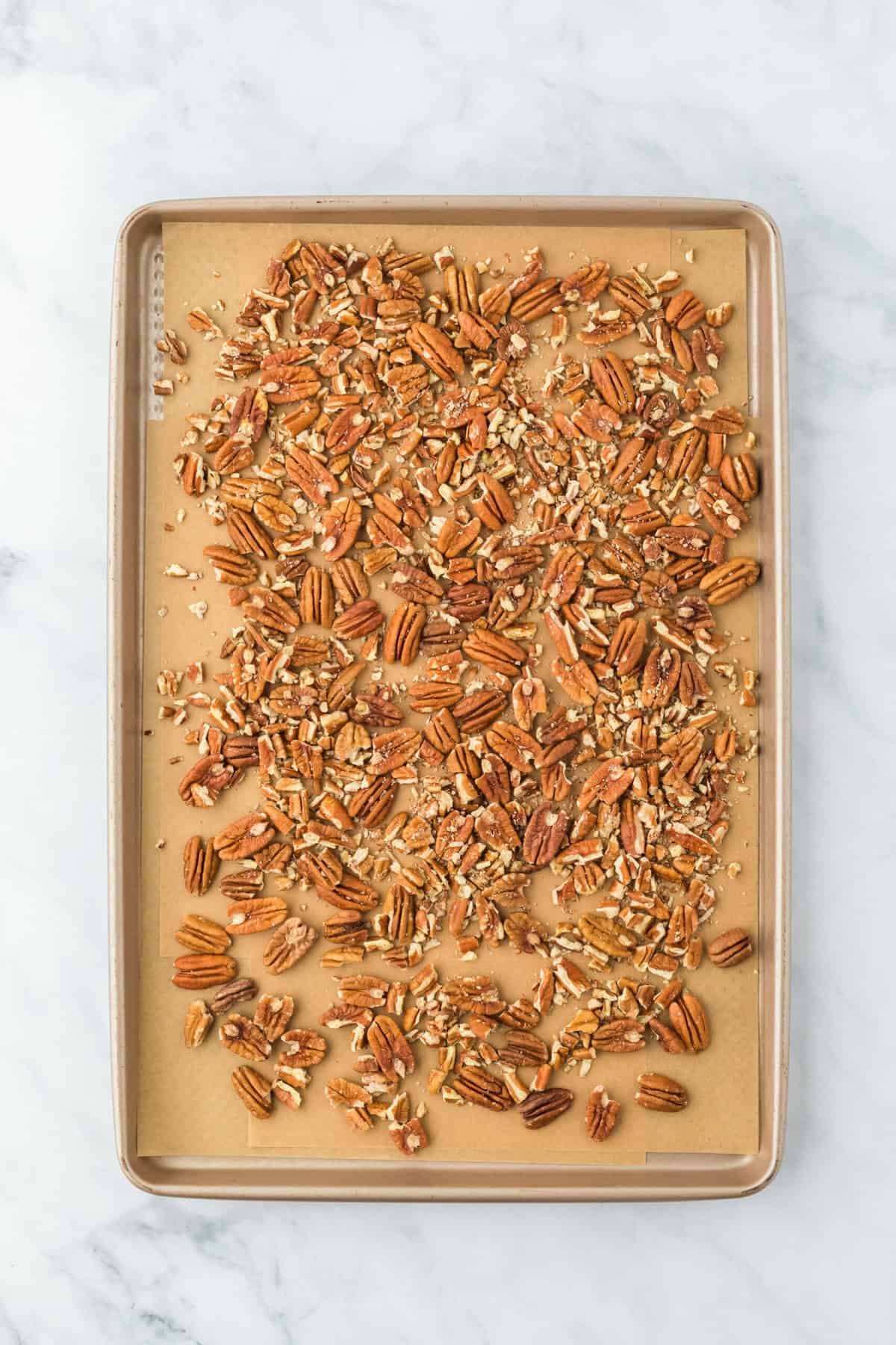 Pecans spread on a parchment lined baking sheet before baking