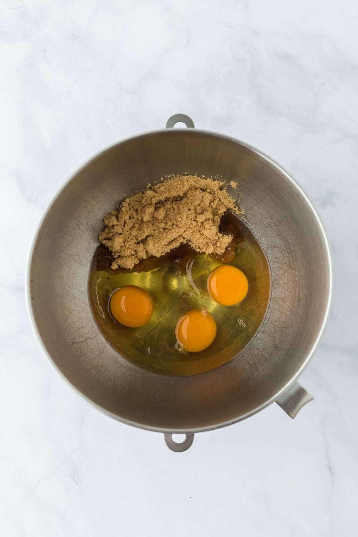 Eggs, corn syrup and brown sugar added to a stand mixer bowl on a white background