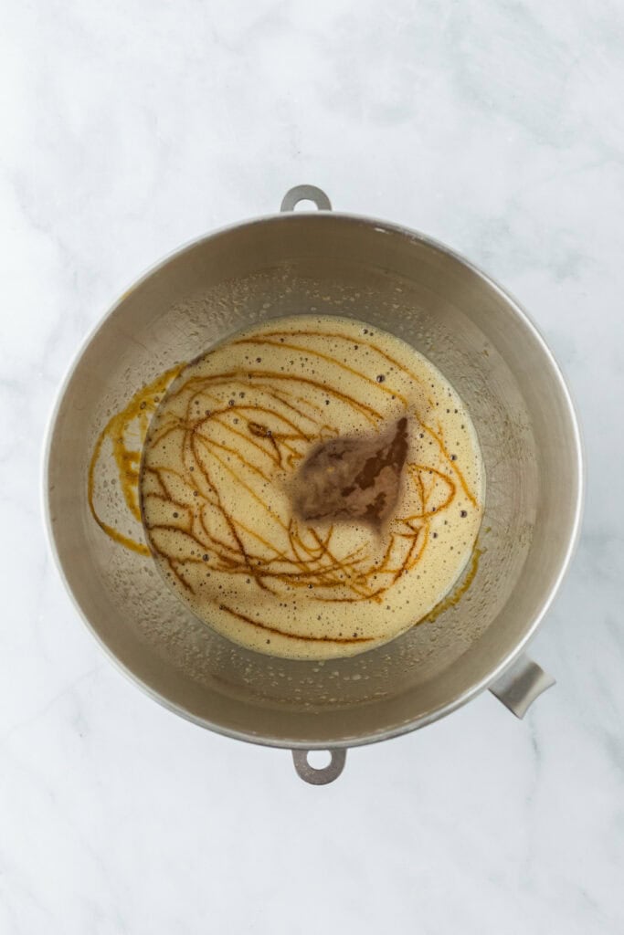 Molasses and vanilla added to a frothy egg mixture in a stand mixer bowl
