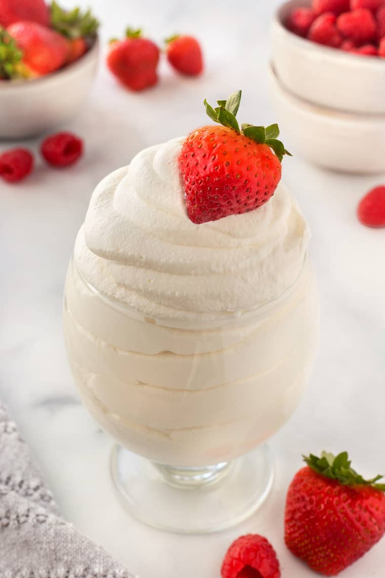 A glass of whipped cream with a strawberry on top and others in the background