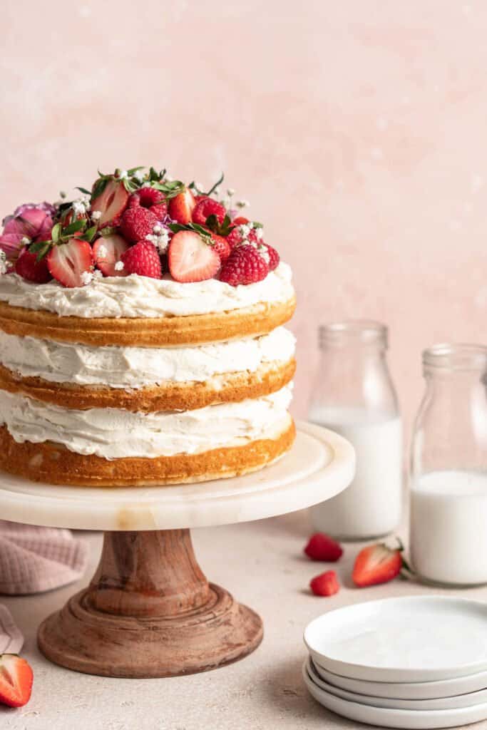 A close up side view of a naked white cake topped with berries