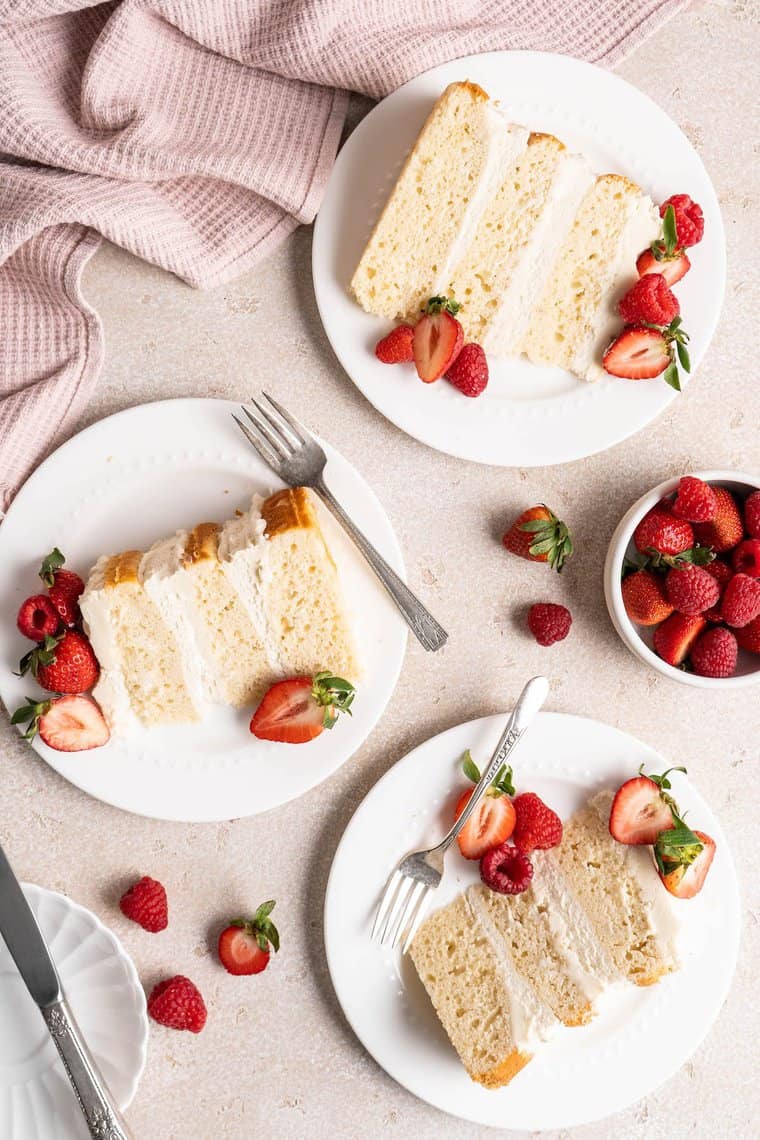 Slices of basic white cake recipe on white plates with berries on top