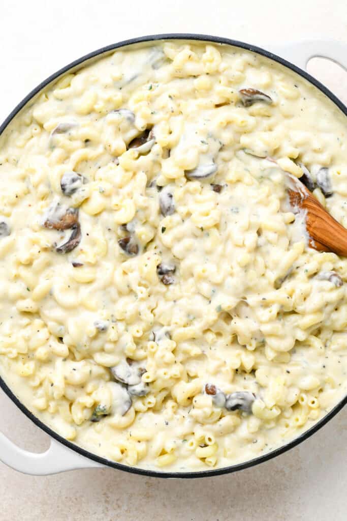 Creamy macaroni and cheese in a large skillet being stirred with a wooden spoon