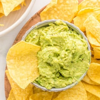 Corn chips on a platter with one inside a bowl with guacamole
