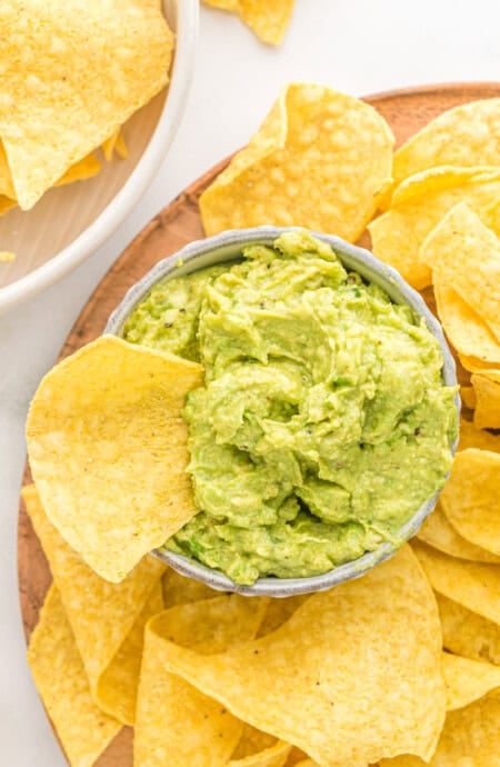 Corn chips on a platter with one inside a bowl with guacamole
