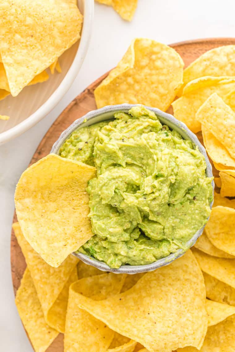 Corn chips on a platter with one inside a bowl with guacamole