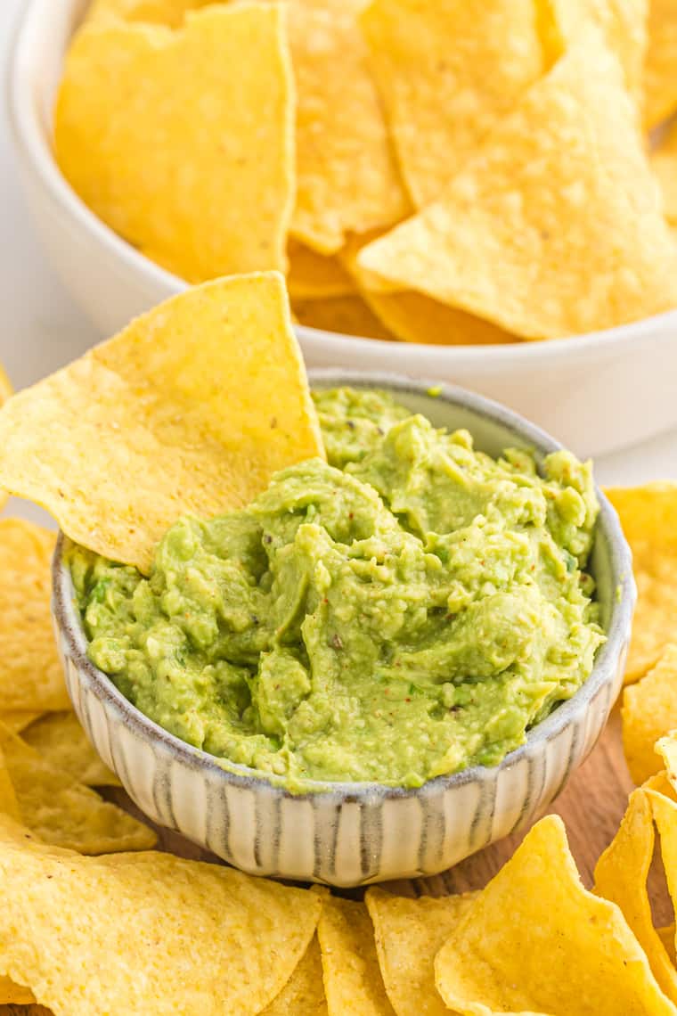 A bowl of guacamole with a corn chip inserted inside