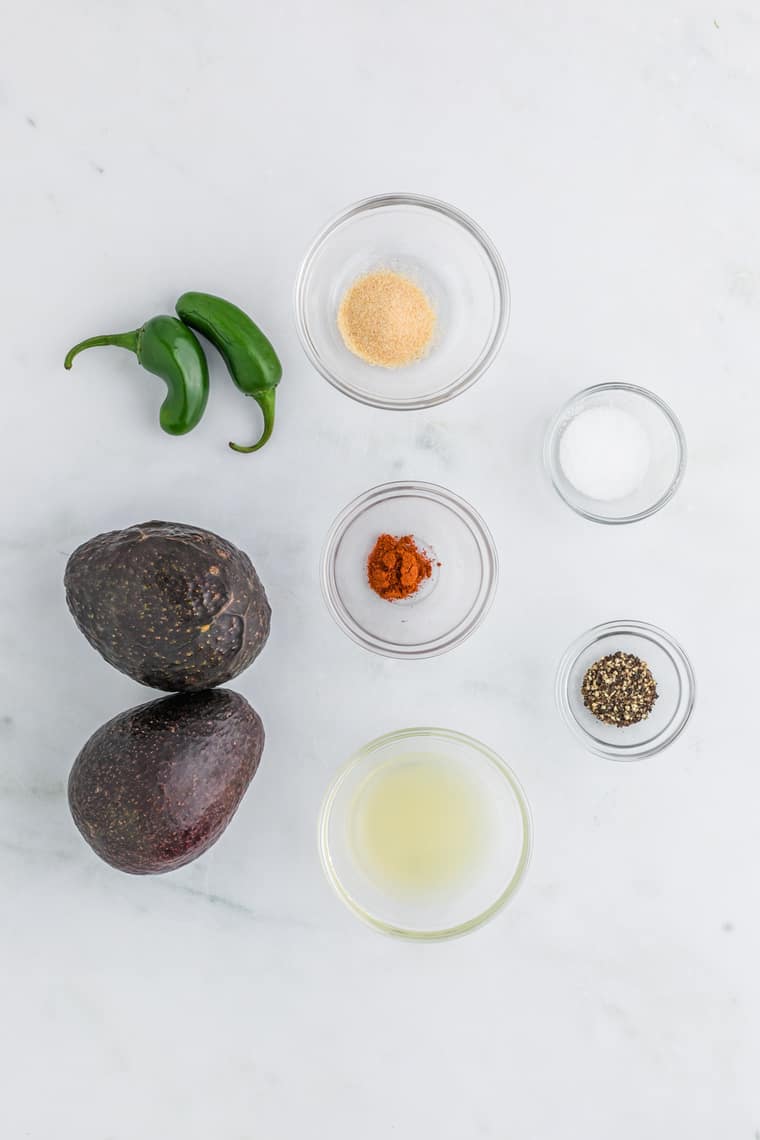 Hass avocados, spices, peppers and lemon juice against a white background