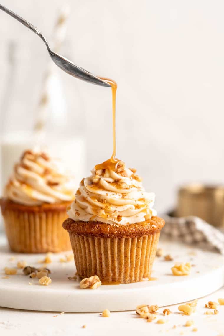 A close up of two cupcakes with one carrot cake cupcake having caramel poured on top