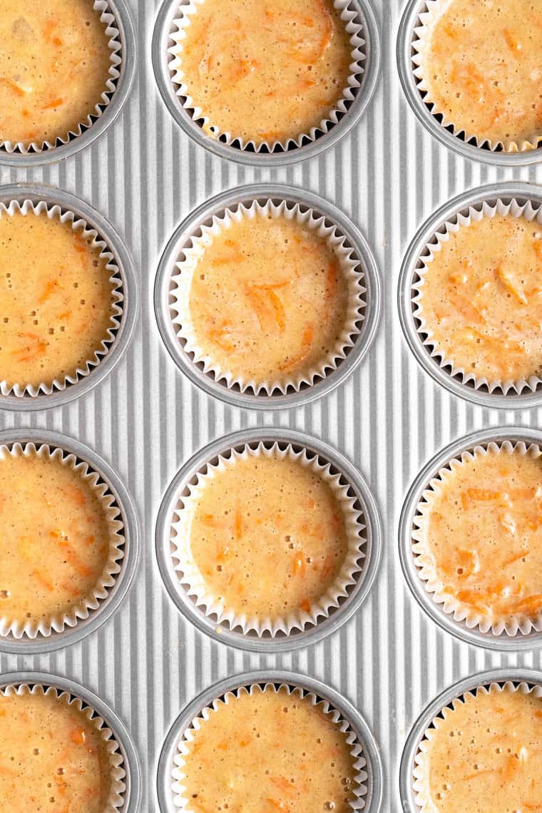 A close up top down view of carrot cupcake batter in liners in a muffin pan before baking