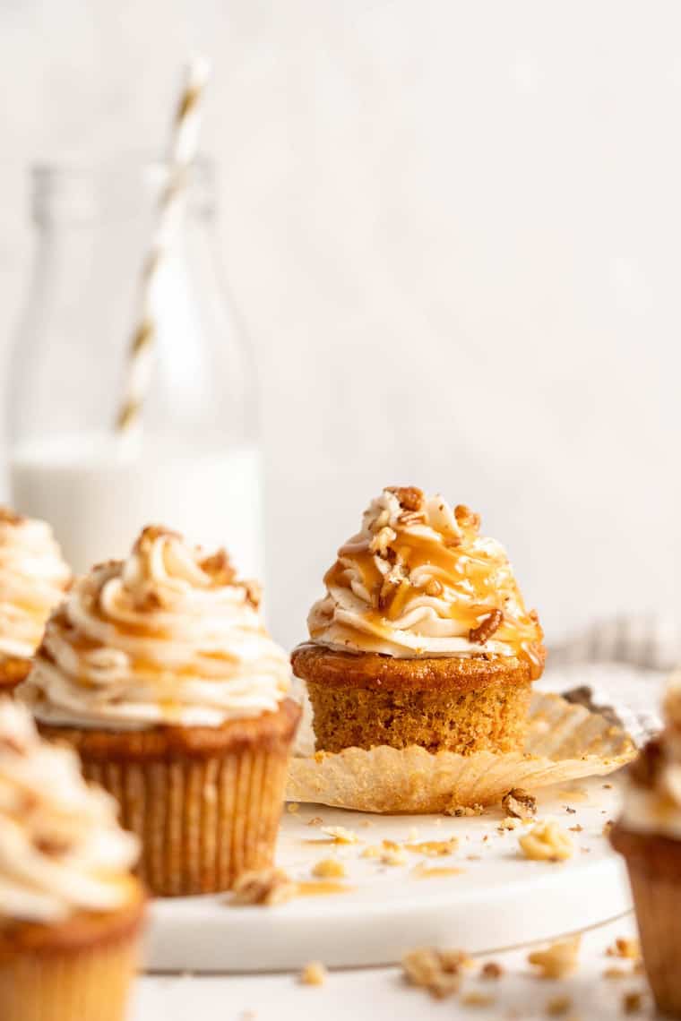 Carrot cupcakes against a white background with caramel sauce and one unfolded from a liner