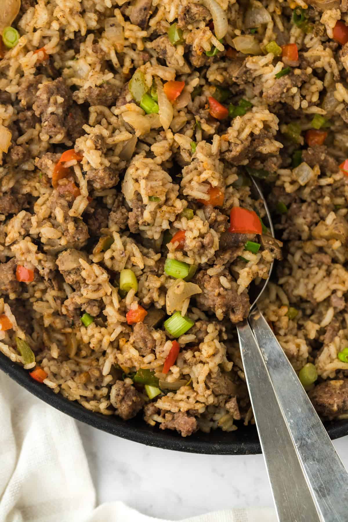 Cajun dirty rice in a large black pot with a large spoon digging in against a white background