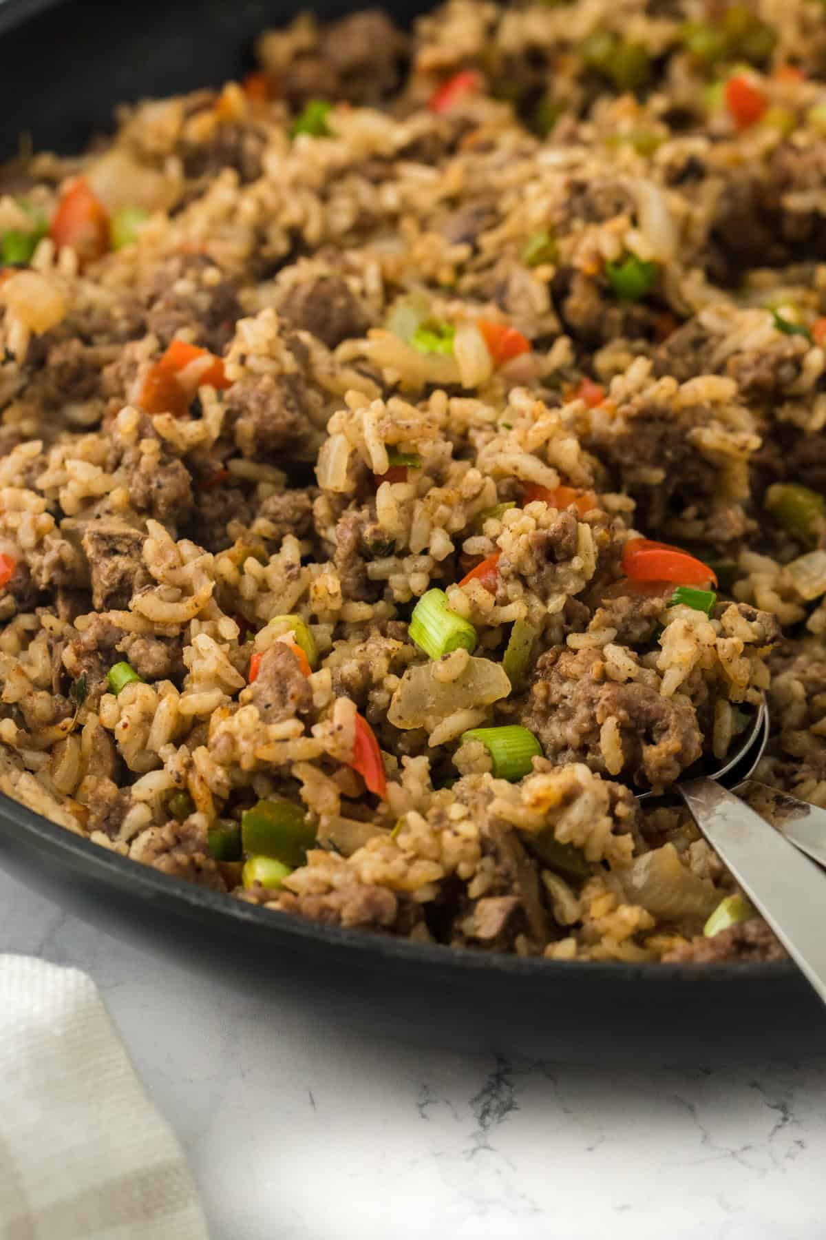 Dirty rice with sausage in a black pan with a spoon scooping some on a white background