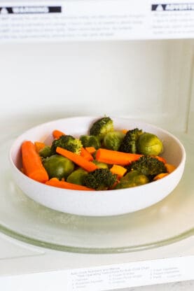 In a tutorial on how to steam vegetables, there is a white bowl of veggies in the microwave