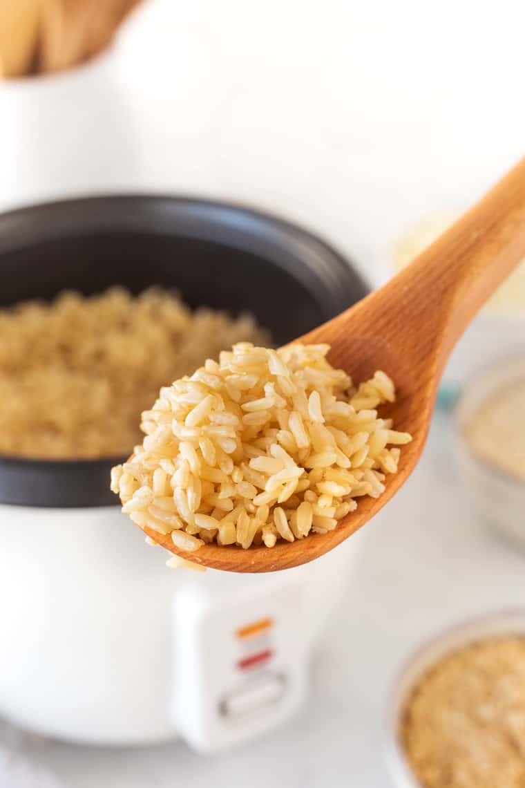 A close up of a wooden spoon with brown rice in a tutorial on how to make rice